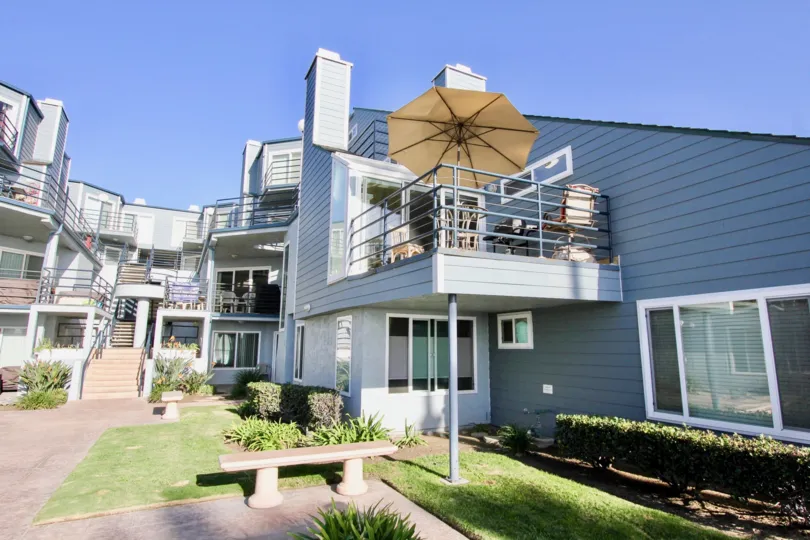 Cement bench near a three story home with a patio & umbrella in Oceanside California at Pacifica Strand