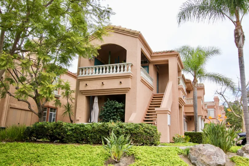 The exterior of the two story Palmilla Del Oro condo complex with exterior stairwells and resident's terraces with palm tree landscaping.