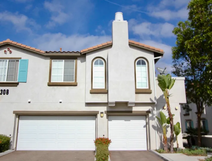A white adobe two story home with two garage doors and a chimney in Pelican Cove