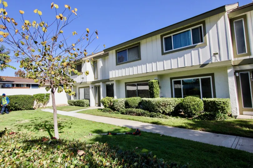Two story white building with windows near grass & plants at Pepperwood Villas in Oceanside CA