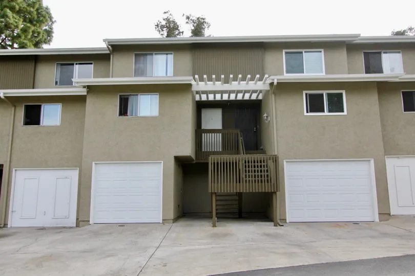Beige stucco duplex home with white accents and backyard greenery.
