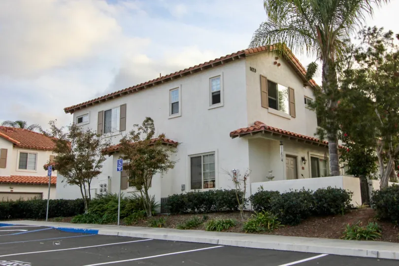 Attached housing unit adjacent to ample parking, with mature trees and half-height privacy fence at Rancho Rose in OCeanside, CA