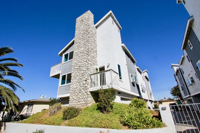 Large white walls and chimney with balcony over looking green foliage.