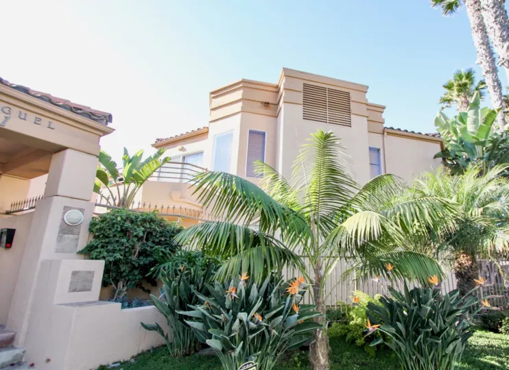 An adobe property with tropical landscaping on a clear day at San Miguel III