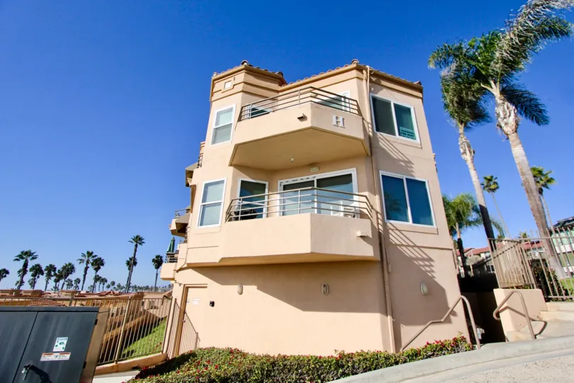 Sunny day overlooking large three story house with tan walls and 2 balconies.