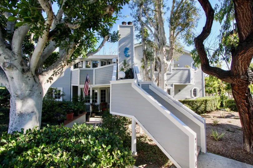 THE BUILDING IN THE SANDPIPER COVE WITH THE UPSTAIRS, TREES, FLAG, WINDOWS, FLOWER WASH