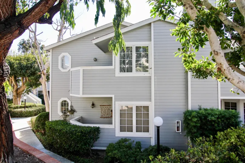 The wood-sided exterior of the two story Sandpiper Cove apartments with private balcony's and bushes.