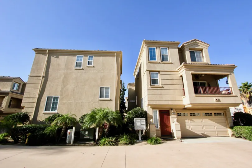 Three story town homes with a large brown garage door next to plants inside Sea Breeze Beach Cottages in Oceanside CA