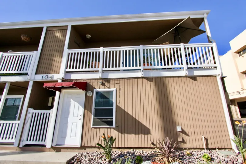 A view of a house with a balcony with a sign 104 at the door and a little garden in front of the house