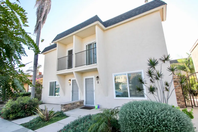 Two story house with railing on patio, gated back yard, and sidewalk in front, located in Six Palms, in Oceanside, California.
