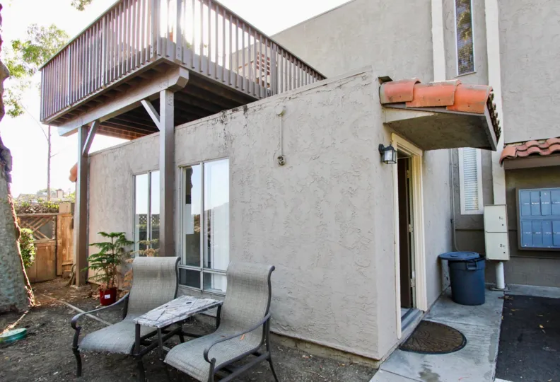 Building with second floor balcony, two chairs and gate beside it, located in Vine Villas, Oceanside, California.
