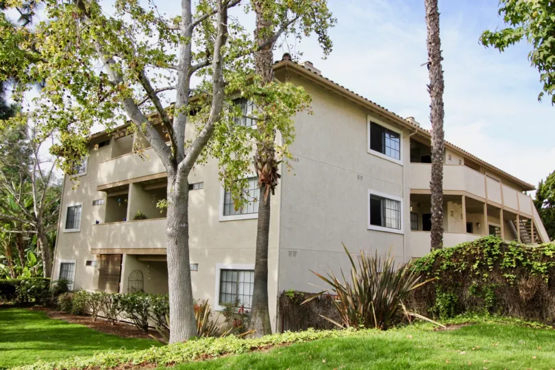 Large white three story home with white and beige and foliage at Vista Way Village.