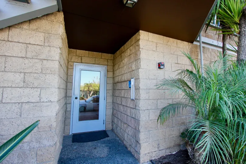 Cinderblock tan front door entrance, angular doorway/building, with overhang in tropical setting with palms, apartment building, intercom buzz-in style system, glass door