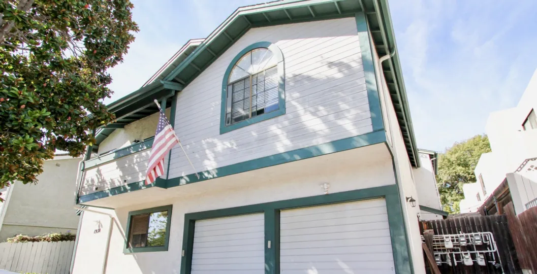An exterior view of a unit at the Baycrest apartment with charming blue trim, private balcony, and patriotic flag.