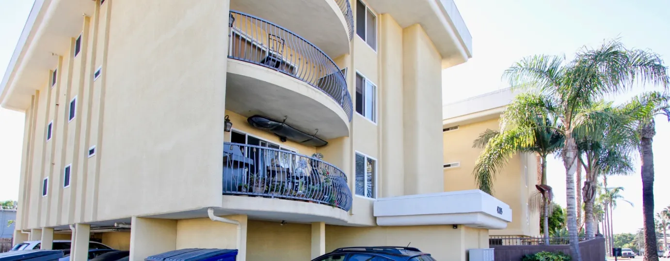 THE BUILDING IN THE BAYVIEW CONDOS WITH THE CAR PARKING, BALCONI, CHAIR, TREES, PLANTS