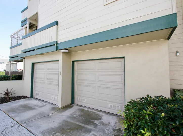 2 garage doors for a multi-story building with bushes on the right and a succulent plant on the left