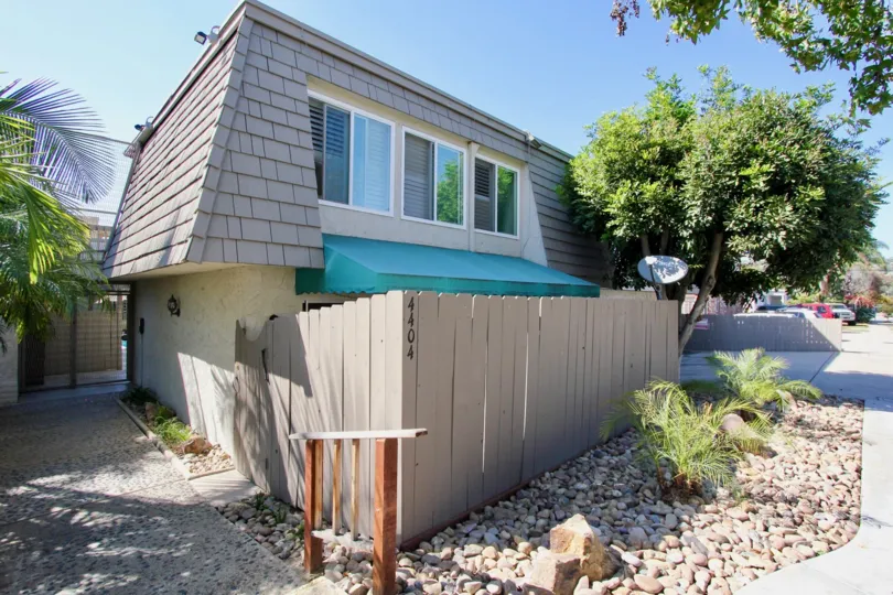 A sunny day in the area of La Casa Villa, outside, wooden fence, rocks, driveway, house, trees
