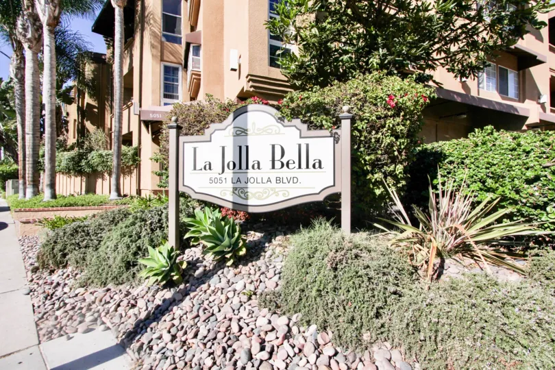 sign of La Jolla Bella welcoming nto the community with lush geenery and housing behind it