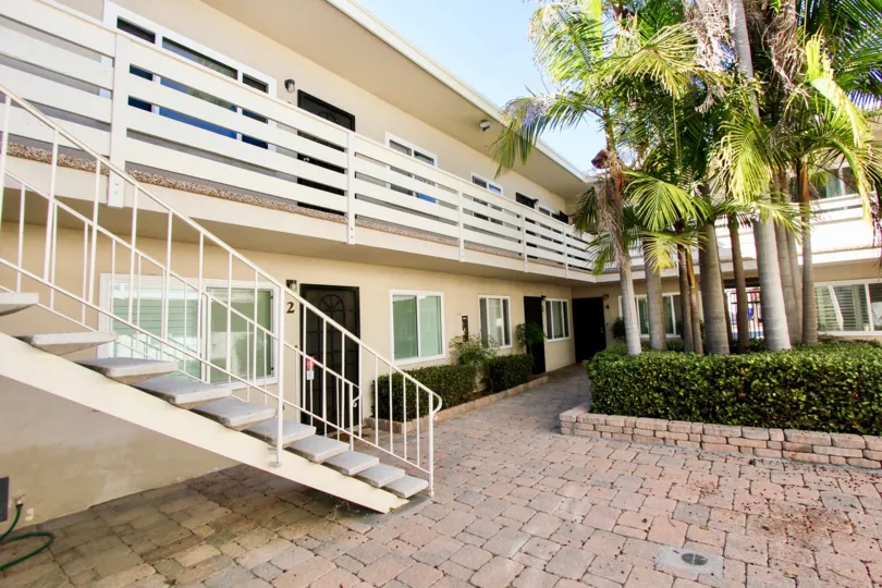 The exterior of the two story Loring Manor apartments showing the bricked terrace, outdoor staircase, and palm tree landscaping.