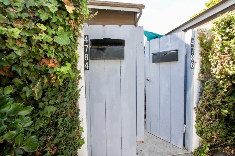 A white wooden gate covered in shrubs in the Pacifica Townhomes community.