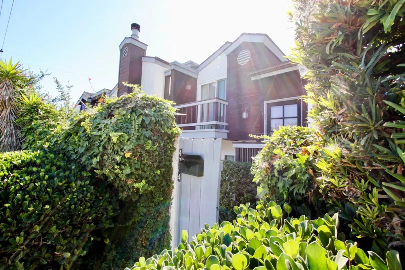 A red and white low-rise townhouse in the Pacifica Townhomes community with an overgrown yard.