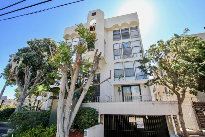 A modern, white apartment building in the San Remo neighborhood in Pacific Beach, CA with shrubs and trees