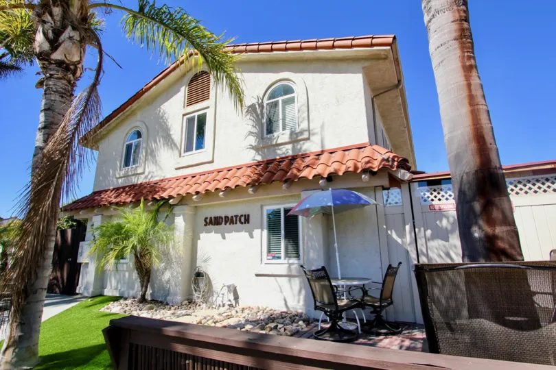 A sunny day in the Sand Patch a beautiful wight color house with lawn and small table and chairs.