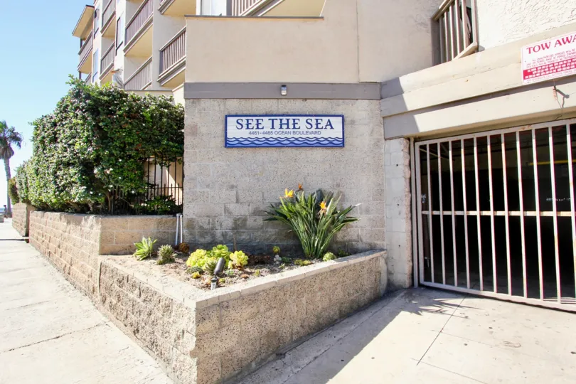 The side of See The Sea apartments and potted plants in front of the sign.