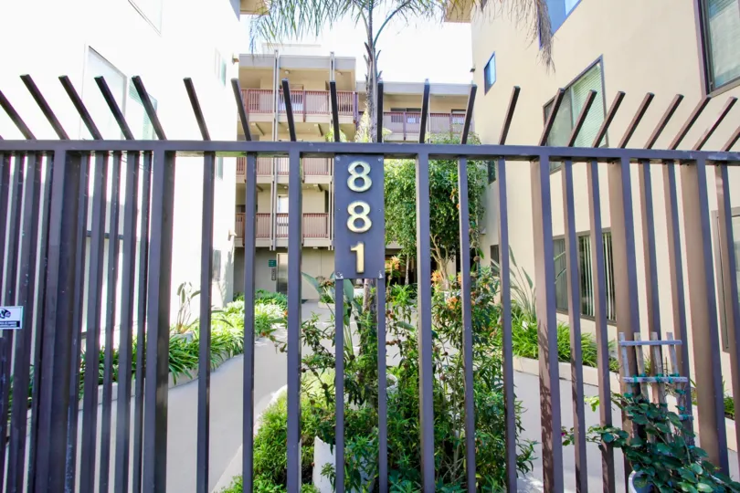 A black colored fence with white and brown colored apartments in the background.