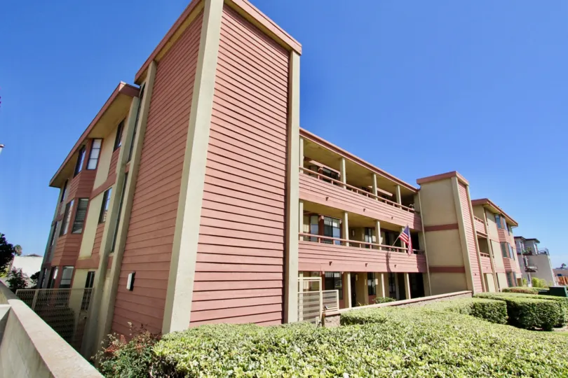 A large pink & brown town home building next to hedges inside Addison Street in Point Loma CA