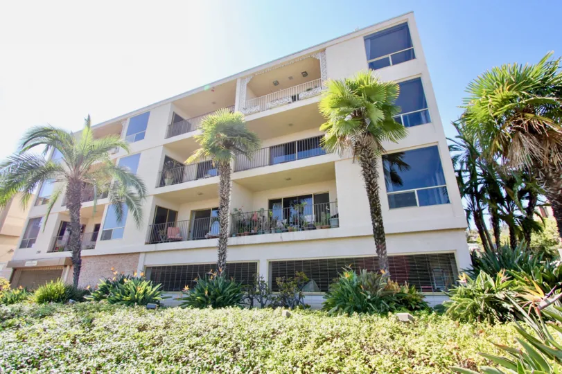 Shuttered shops beneath multi-unit dwellings with balconies surrounded by palm trees in Point Loma, CA