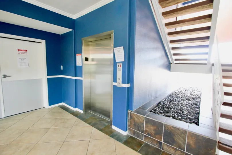 Open riser stairs and tiled floors and stainless steel elevator door in the lobby of the Yacht Club Condos