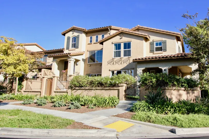 A big house with lots of bushes in front and some trees to the sides during a sunny day in Amante Ravenna, Rancho Bernardo, CA