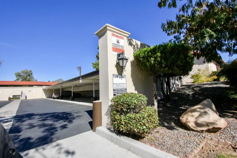 The entrance to a parking lot with a car parked inside and some bushes on the side during a sunny day in Bernardo Villas, Rancho Bernardo, CA