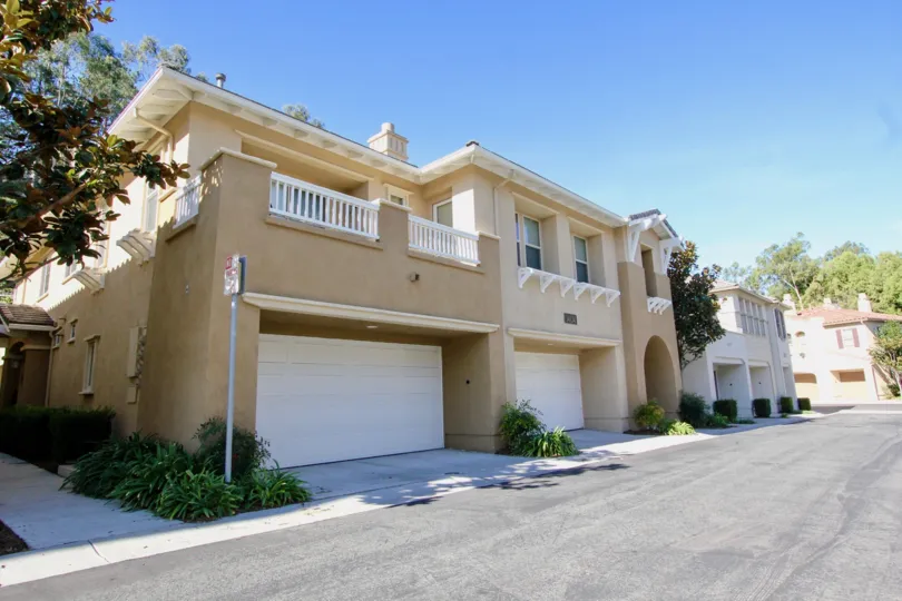 A sand and white colored house with some bushes and a street in front in Cypress Greens, Rancho Bernardo, CA