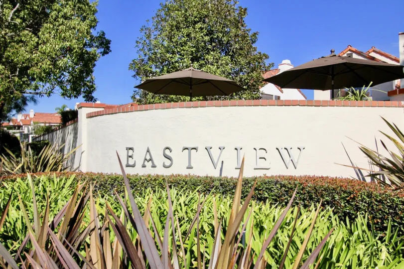 A sign saying "Eastview" with some bushes and trees around it and shade umbrellas and houses in the back during a sunny day in Eastview, Rancho Bernardo, CA