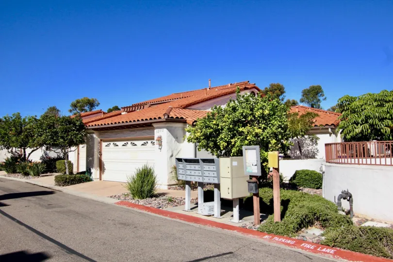 A white house with red roof with some bushes, mailboxes and a street in front at Fairway Vistas, Rancho Bernardo, CA