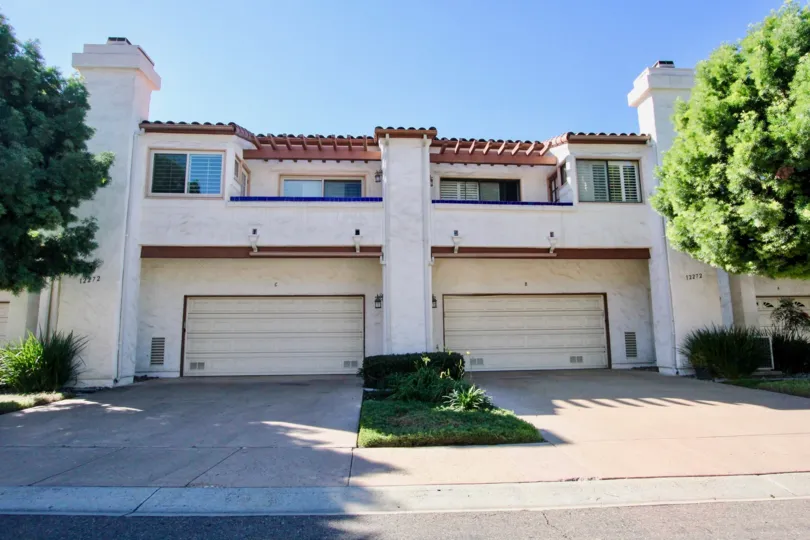 A duplex white house with two garages and some bushes in front during a sunny day in Fairway Vistas, Rancho Bernardo, CA