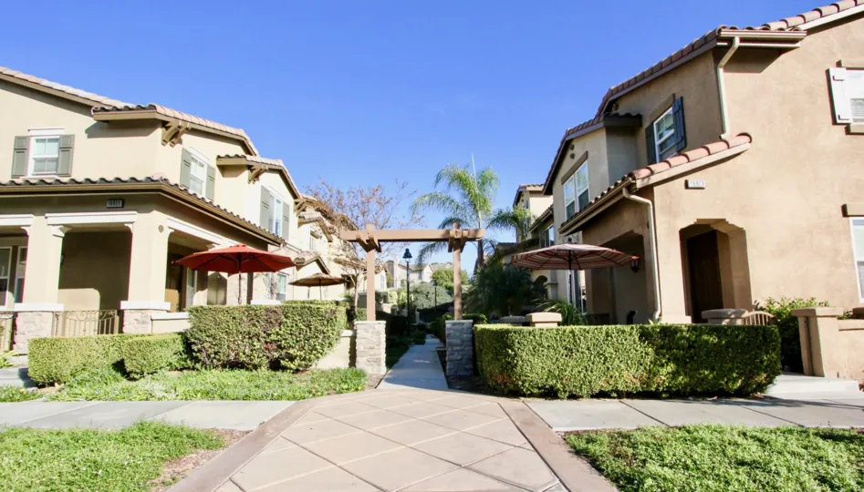 A pathway in between lines of houses with some bushes in front during a sunny day in Garretson in Del Sur, Rancho Bernardo, CA