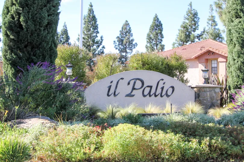 Black writing on a white sign surrounded by plants at II Palio in Rancho Bernardo CA