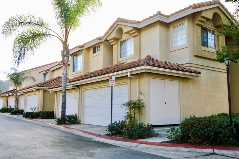 A row of yellow houses with red roofing with a palm tree on the side and some bushes in La Cresta, Rancho Bernardo, CA