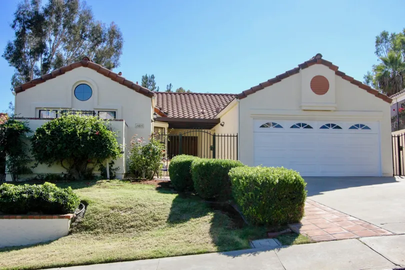A beige house with a white garage and some bushes in front during a sunny day in Las Brisas, Rancho Bernardo, CA