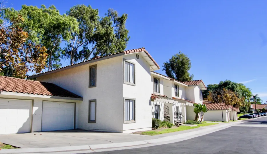 A big house with a garage and a lawn with some bushes and trees in the background during a sunny day in Lomas Bernardo, Rancho Bernardo, CA