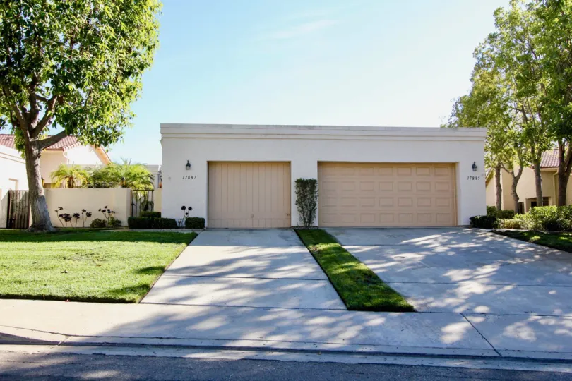A white and brown house surrounded by bushes, trees and tall grass during a sunny day in Oaks North Villas, Rancho Bernardo, CA
