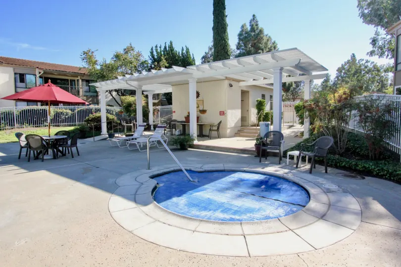 On a sunny day, One Oaks North with dining table and children's pool with tall trees