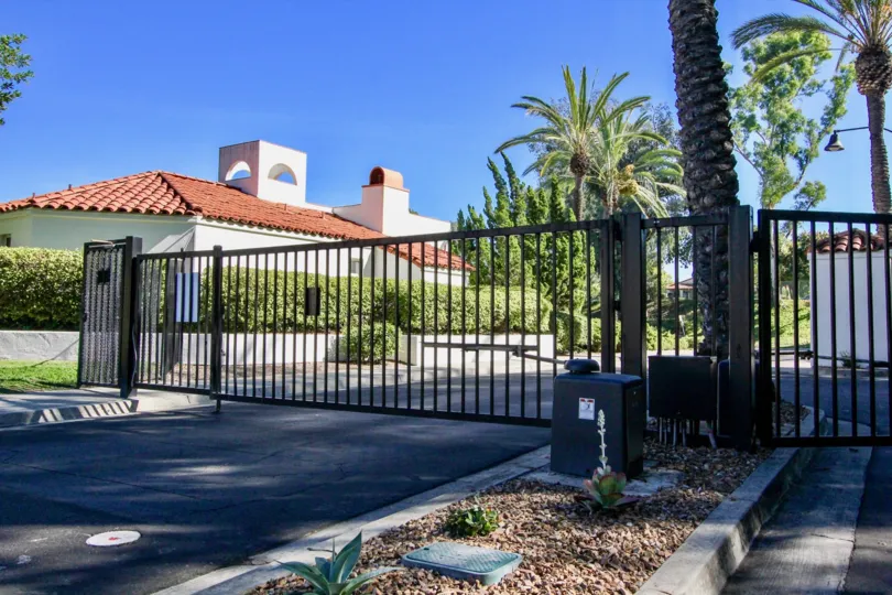 A gate with some palm trees and a house in the background during a sunny day at Palazzo Bernardo, Rancho Bernardo, CA