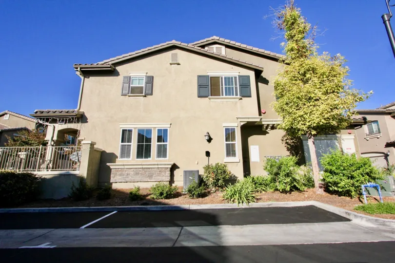 A sandy house with a tree and some bushes in front during a sunny day in Ravenna, Rancho Bernardo, CA