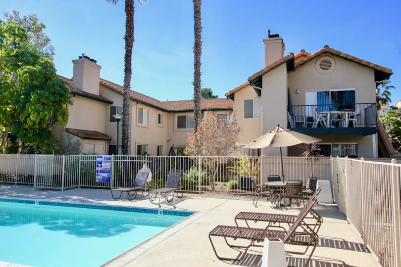 Blue swimming pool with patio chairs and fence at The Falls in Rancho Bernardo CA