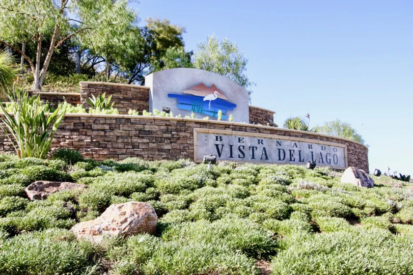 The welcoming sign of rancho bernardo surrounded by trees and plants. the logo of the ranch is a flamingo