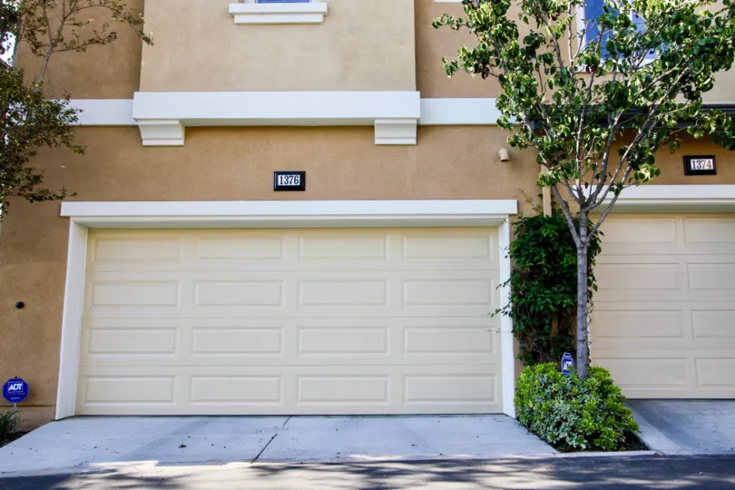 view of a garage door of a house, cream door a tree on right
